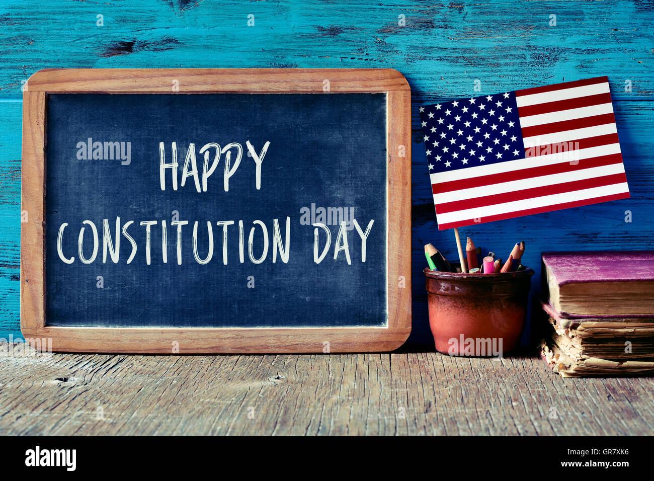 a chalkboard with the text happy constitution day written in it, a pot with pencils, the flag of the United States and some old Stock Photo