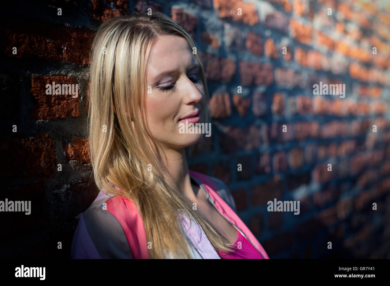 Dreamy Young Woman Leaning In The Light Of The Setting Sun On A Brick Wall. Stock Photo