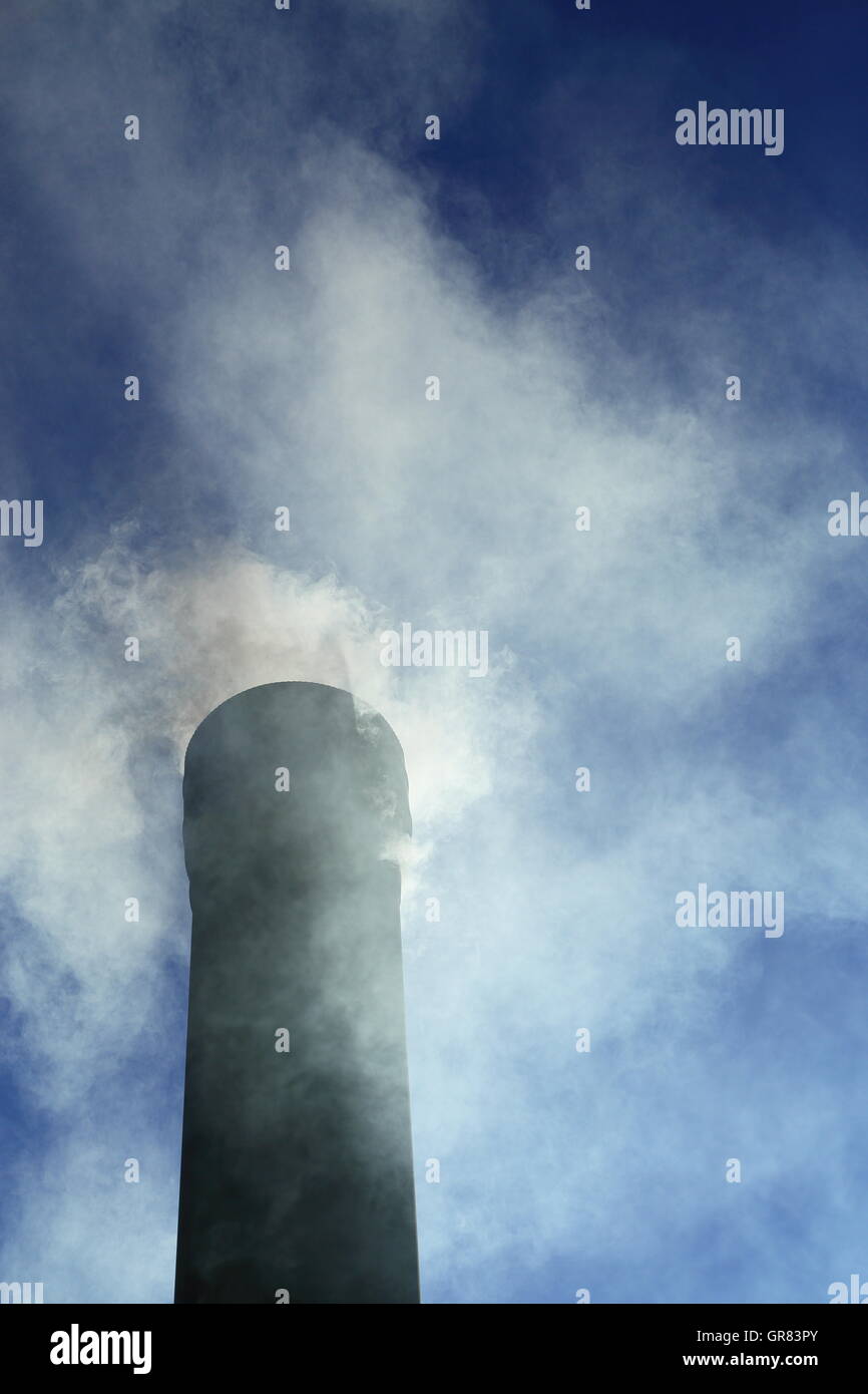 Smoke pours out of a chimney under a vibrant clear blue sky. CO2 emissions are high on current concerns regarding climate change Stock Photo