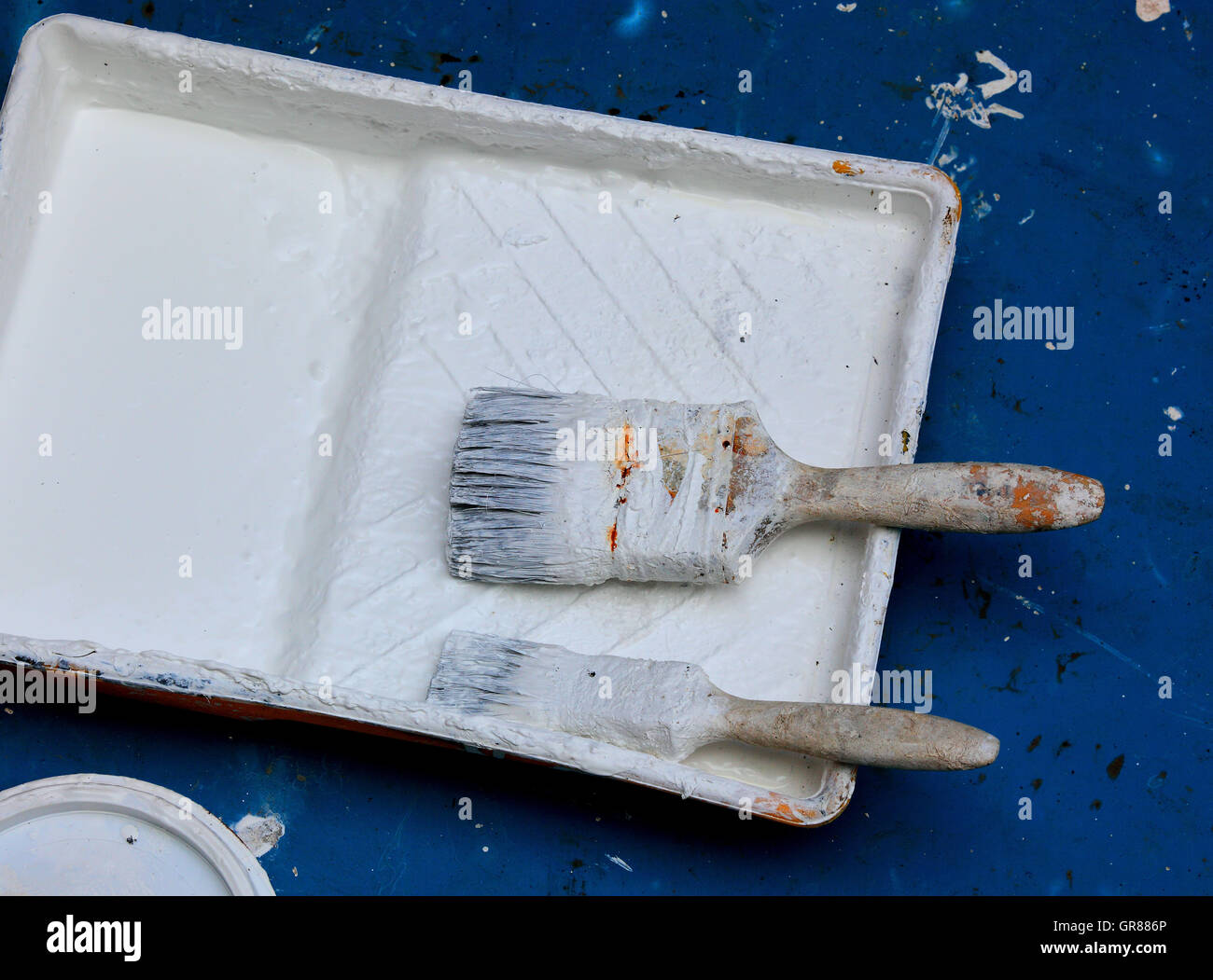 Two white paintbrushes lie in a white colour tub on blue subsoil Stock Photo