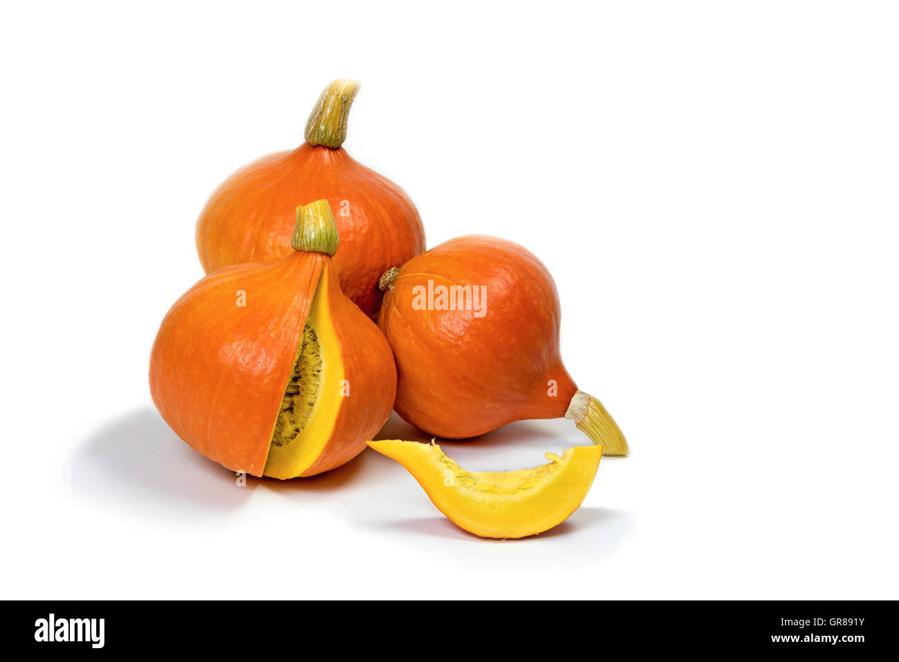 Three pumpkins are lying on a white background. One pumpkin is sliced ...