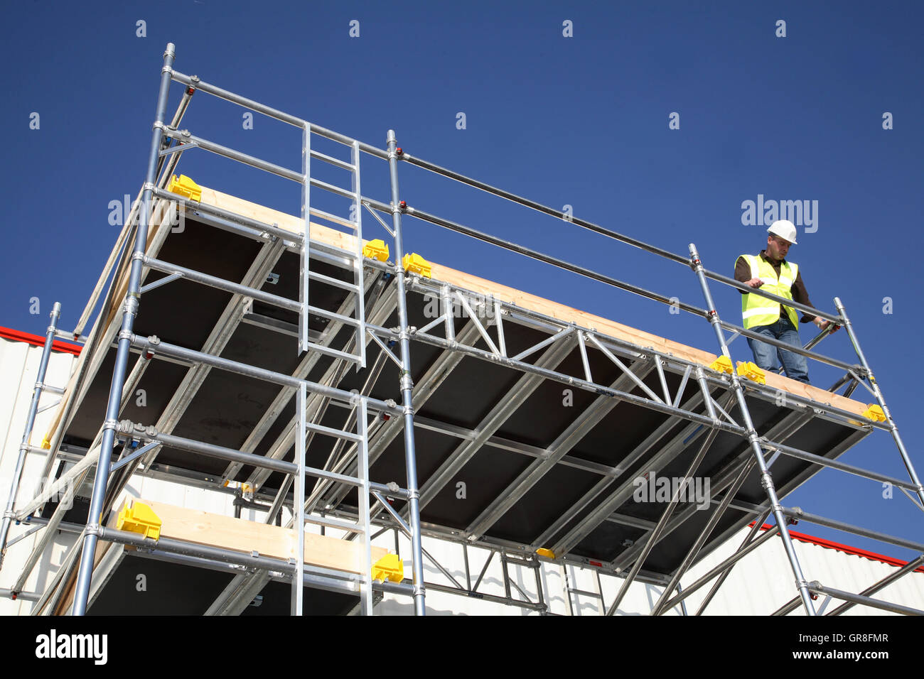A workman stands on a large scaffolding work platform created using an aluminium tower system