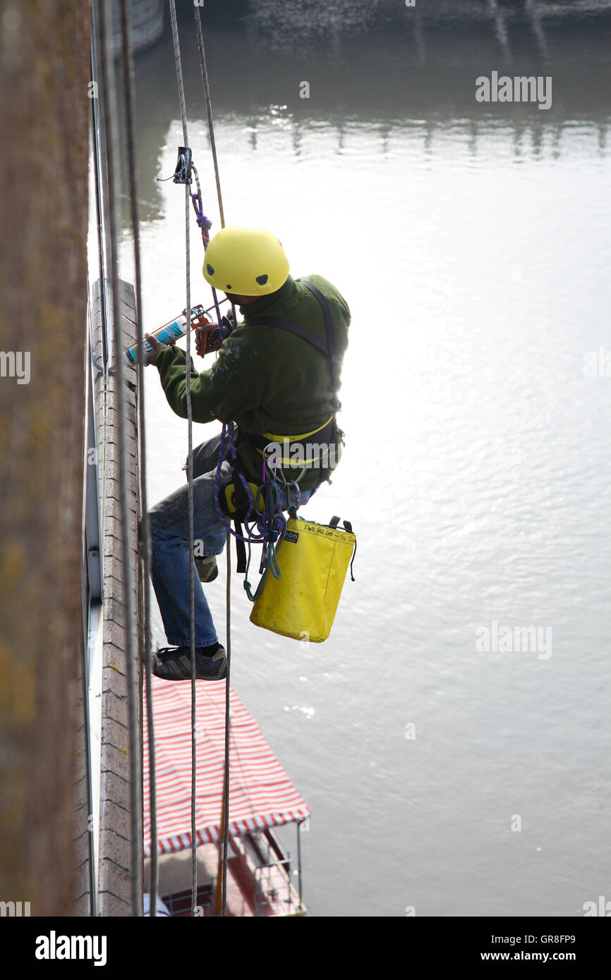 An abseiler uses rope access to place sealant around around windows on ...