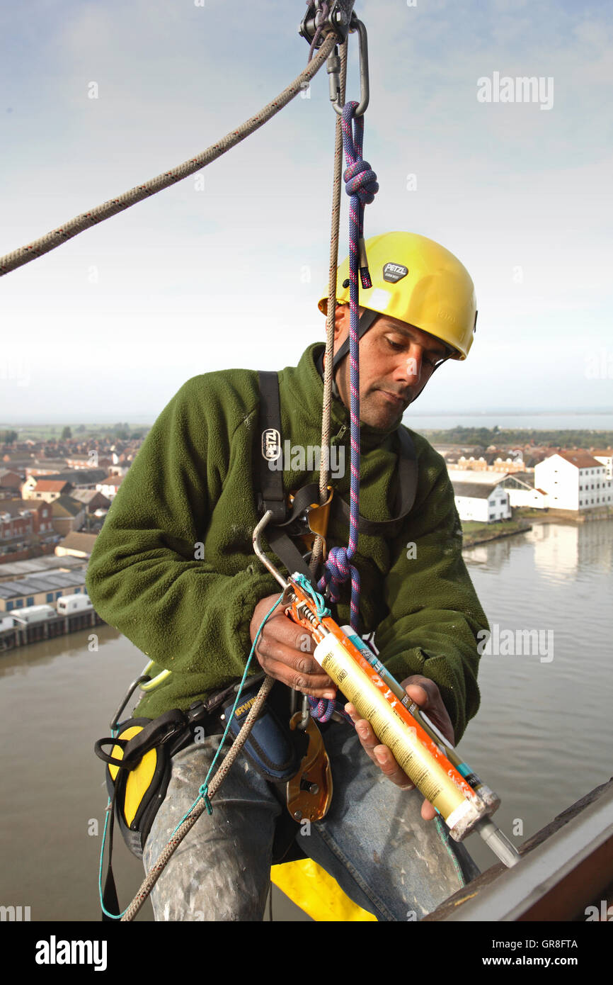 An abseiler uses rope access to place sealant around around windows on