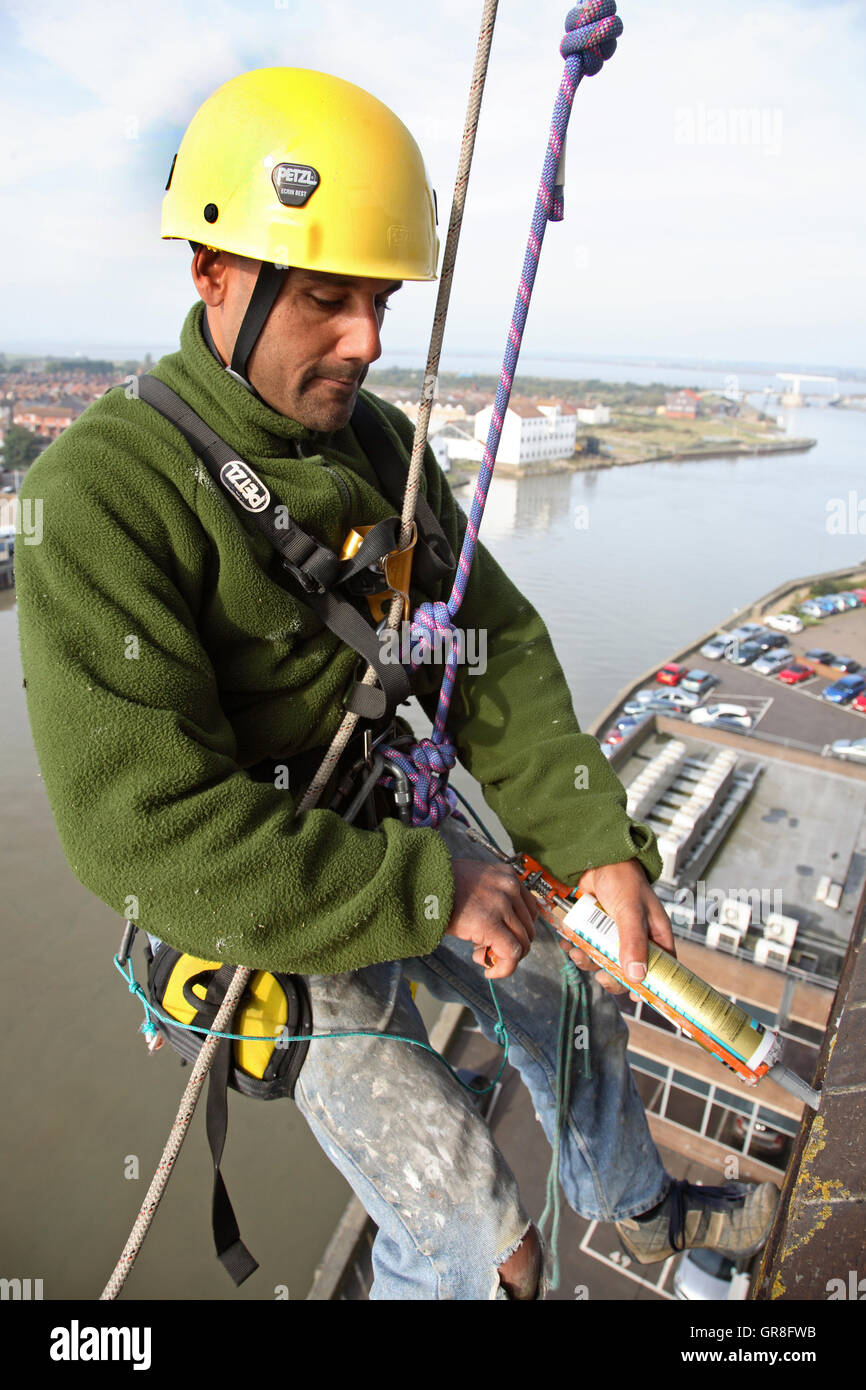 An abseiler uses rope access to place sealant around around windows on ...