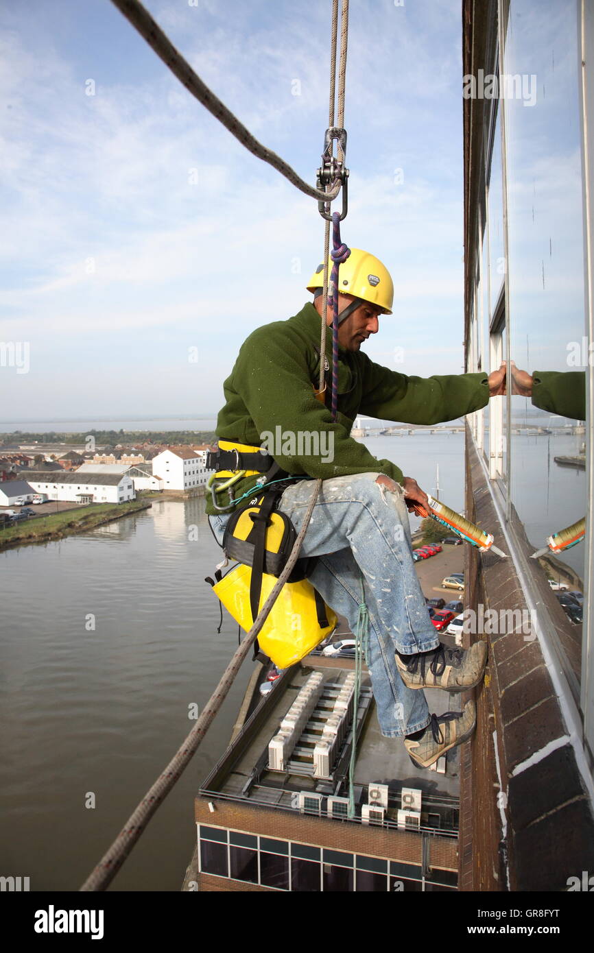 An abseiler uses rope access to place sealant around around windows on ...