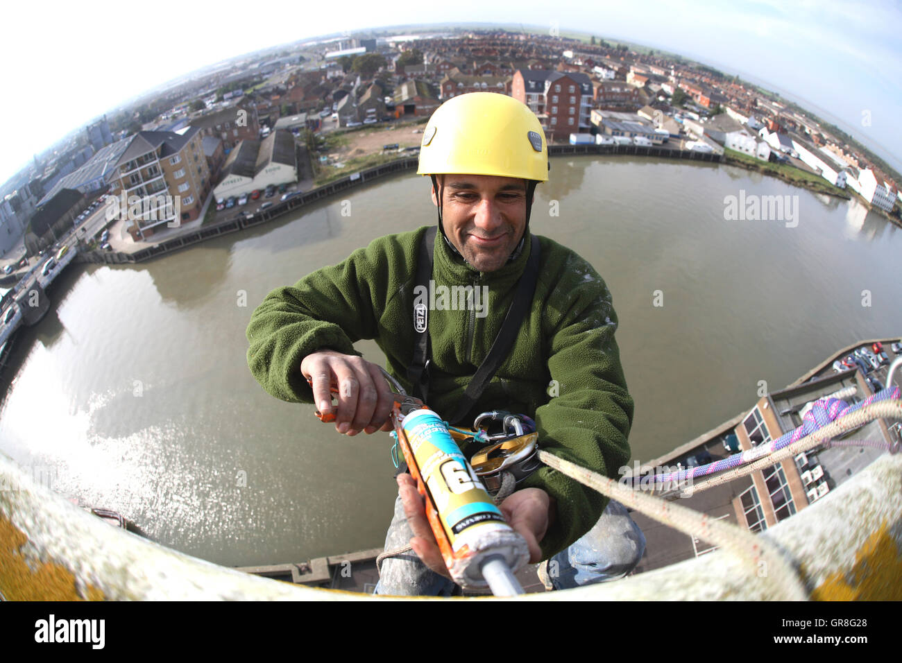 Fish-eye shot of an abseiler using rope access to place sealant around ...