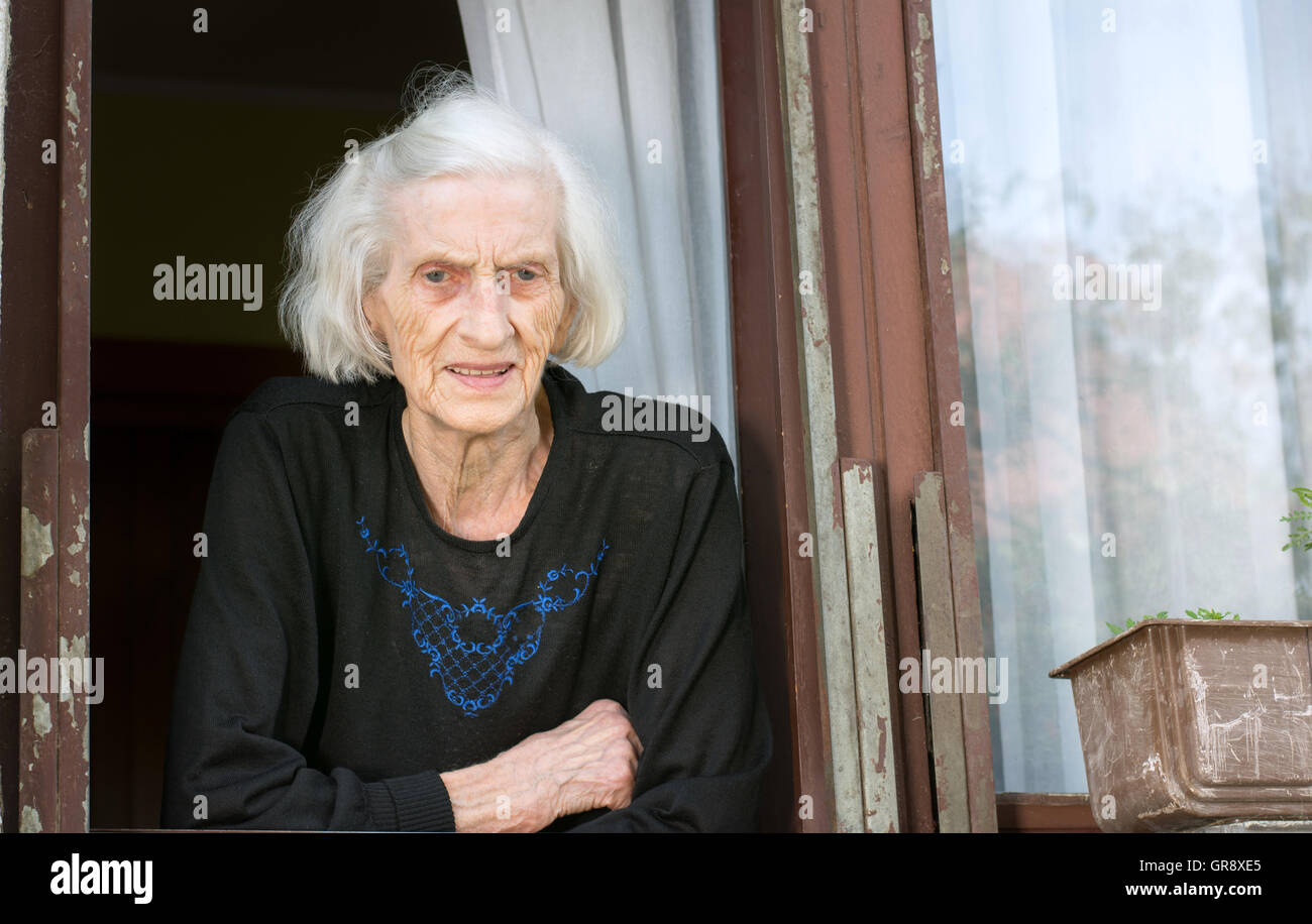 Senior woman alone on her house window Stock Photo