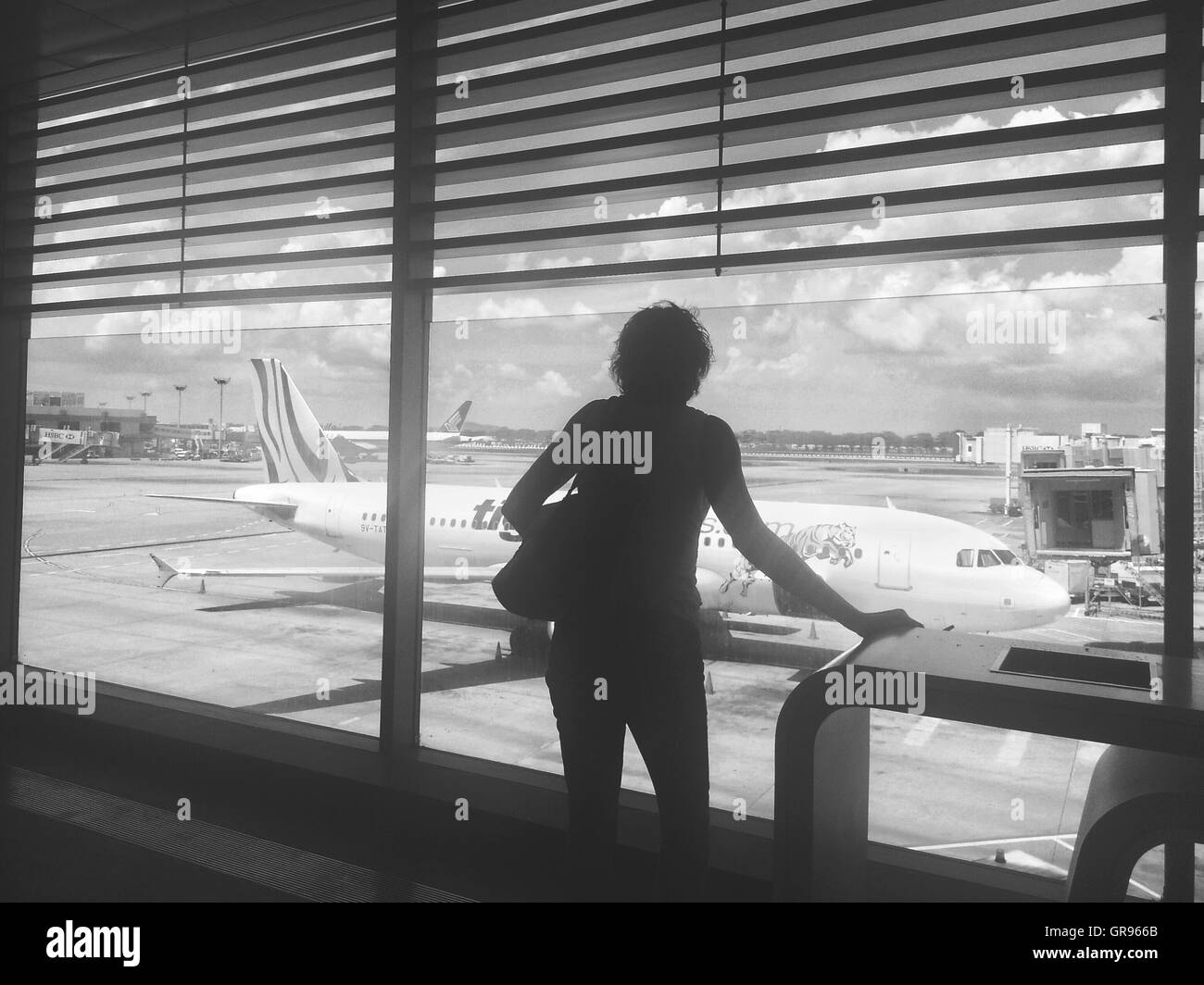 Rear View Of Woman Looking At Airplane On Runway Through Glass Window At Airport Stock Photo