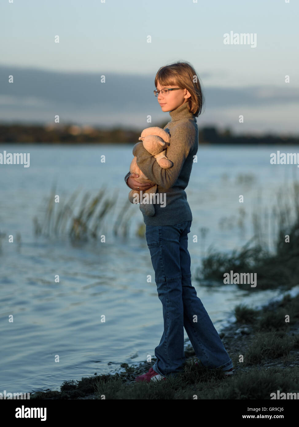 girl teenager stands with a toy and looks at the sunset on the lake Stock Photo