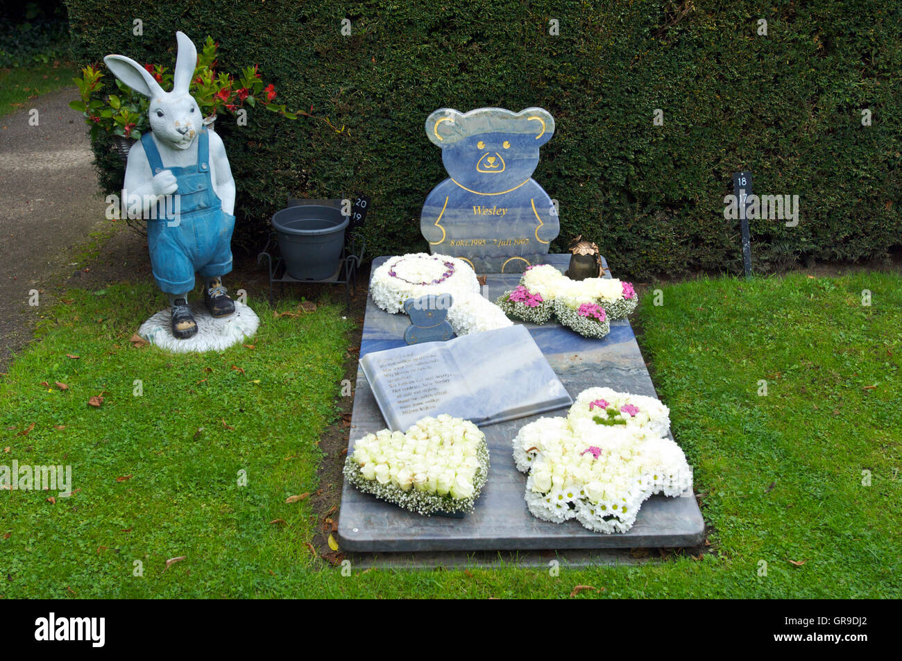 The grave of a child with a statue of a rabbit with flowers in it Stock Photo