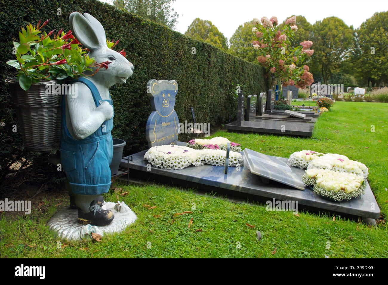 The grave of a child with a statue of a rabbit with flowers in it Stock Photo