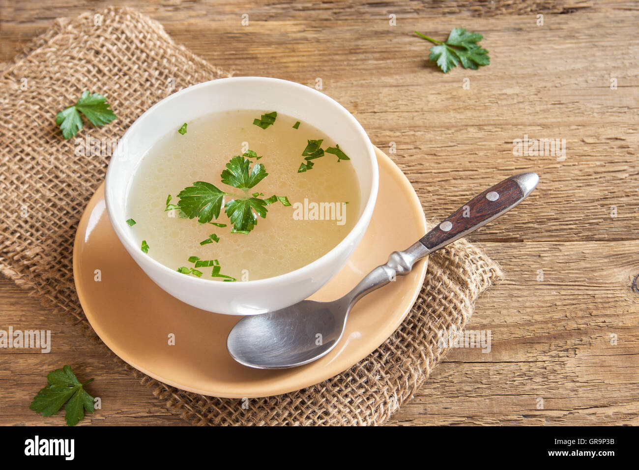 Chicken broth with parsley in white bowl over wooden background with copy space Stock Photo