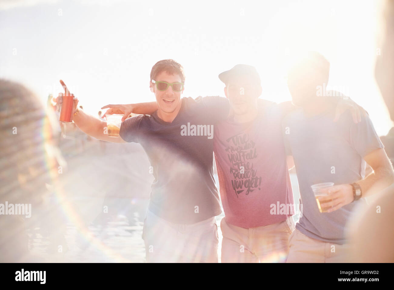 Portrait young men drinking beer at sunny poolside party Stock Photo