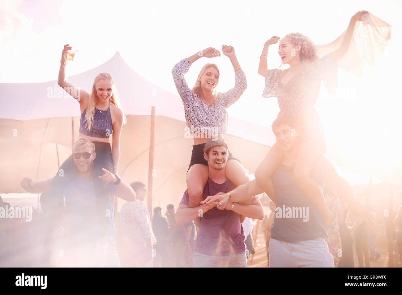 Young men carrying playful women on shoulders at music festival Stock Photo