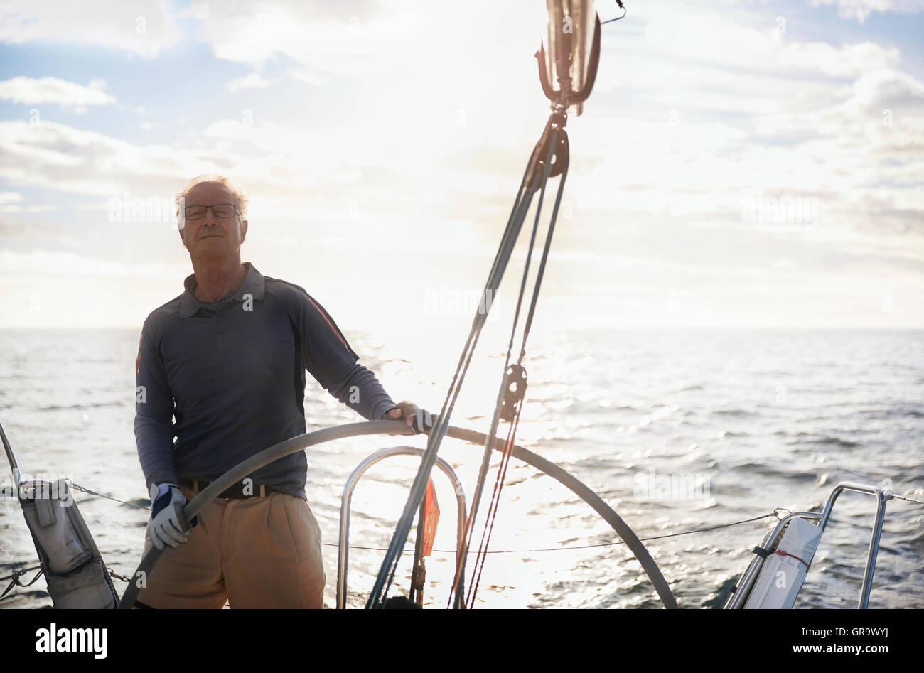 Retired man sailing steering sailboat at helm Stock Photo