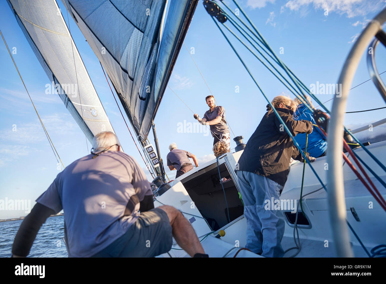 Men sailing adjusting rigging and sail on sailboat Stock Photo
