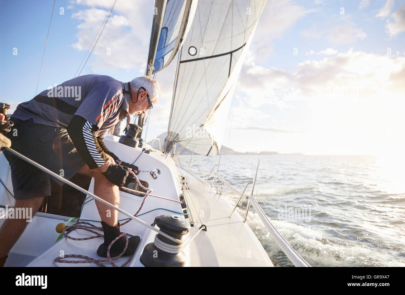 Man sailing pulling rigging on sailboat on sunny ocean Stock Photo