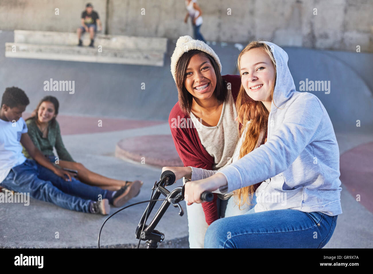 Portrait smiling teenage girls with BMX bicycle at skate park Stock Photo