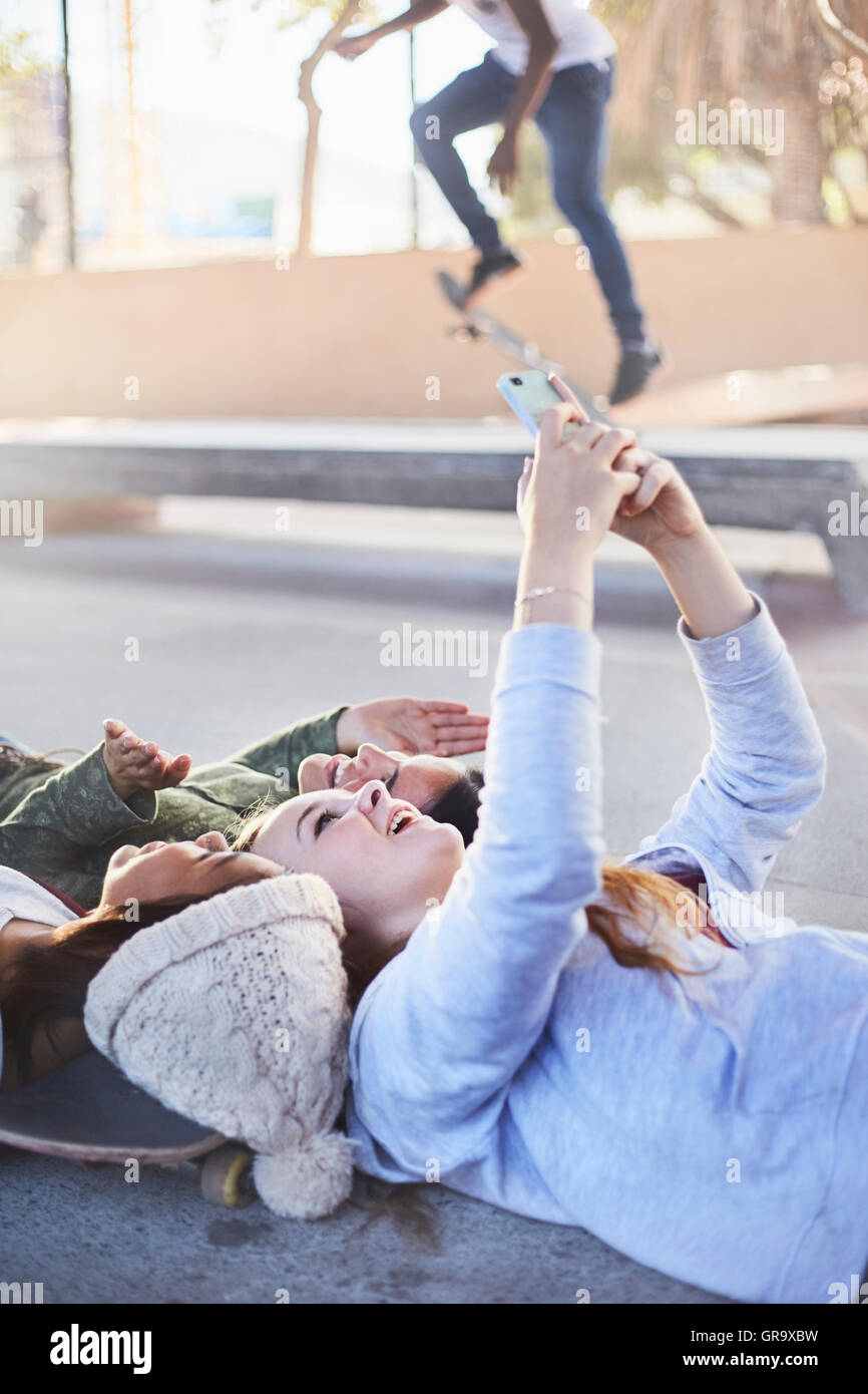 Teenage girls laying taking selfie with camera phone at skate park Stock Photo