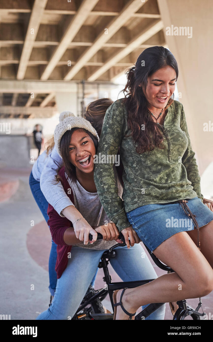 Playful teenage girls riding BMX bicycle at skate park Stock Photo