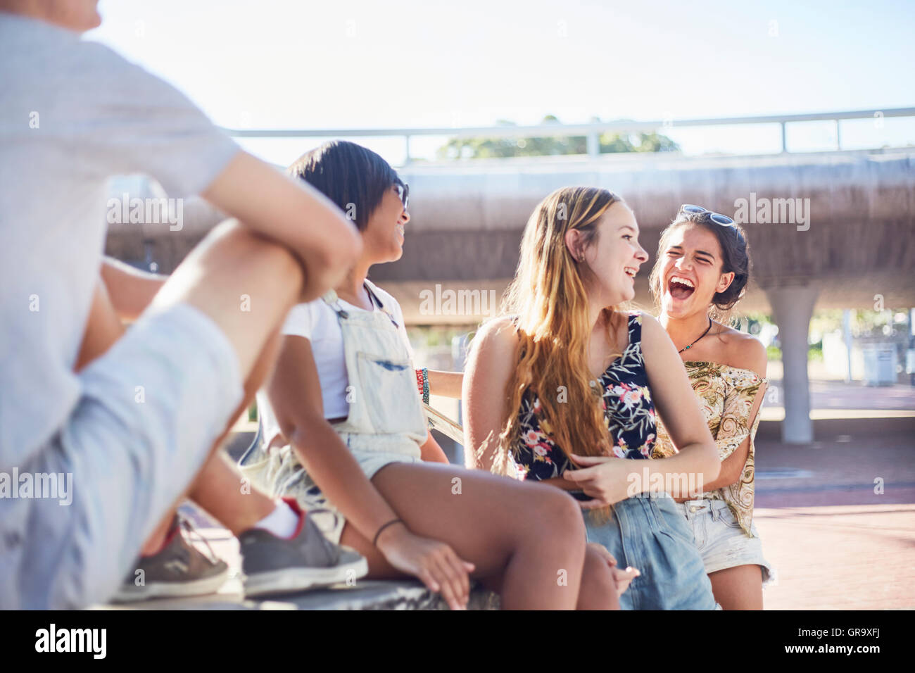 Teenage girls laughing hanging out at sunny skate park Stock Photo