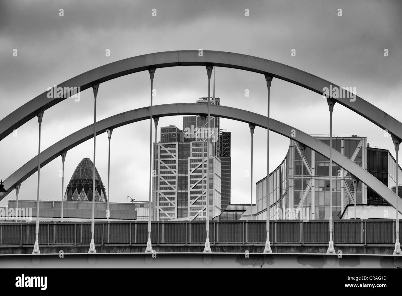 View of the Gherkin and surrounding buildings under cloudy sky framed by arched bridge in London in September Stock Photo