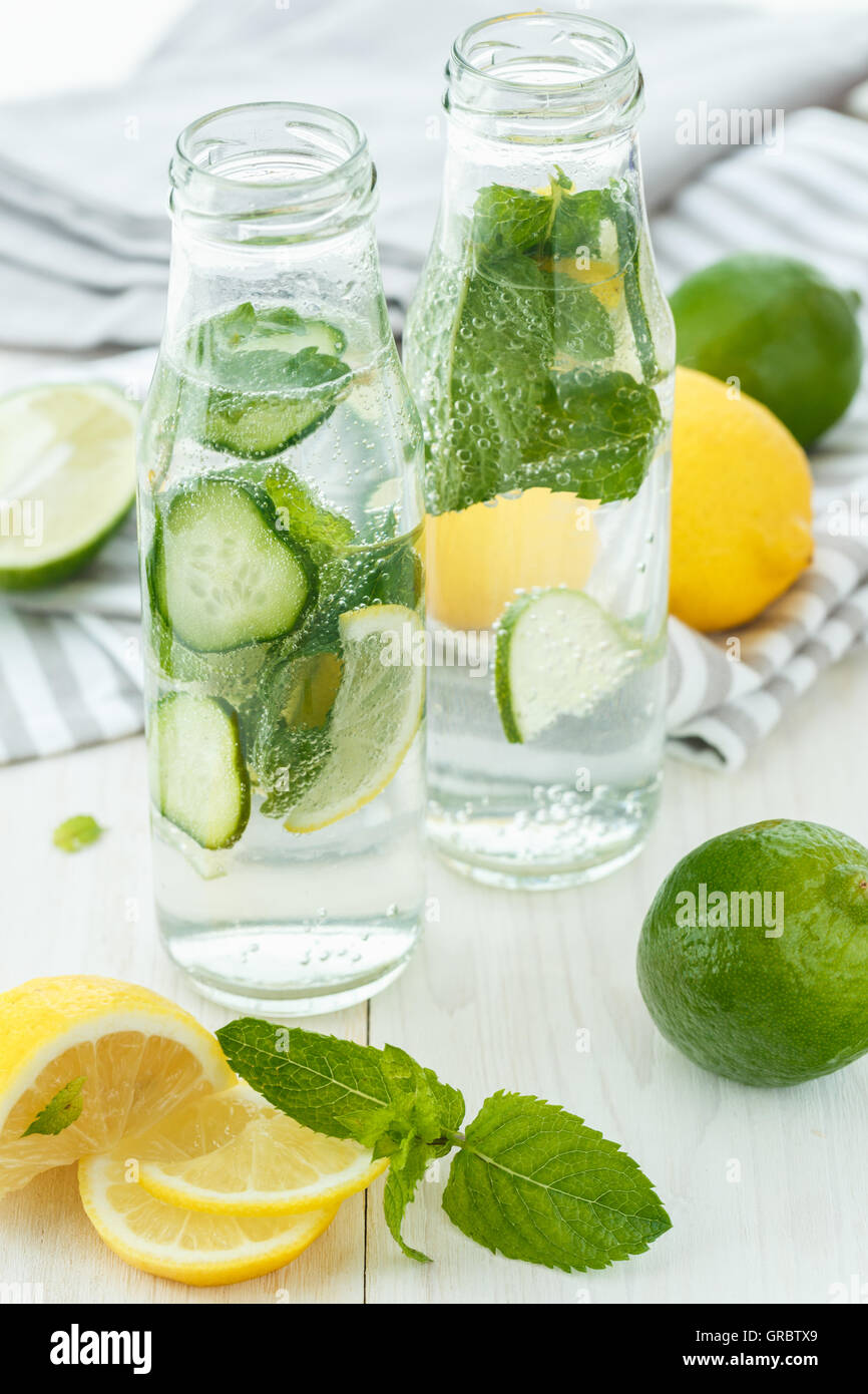 Infused water with citrus and mint in glass bottles on white wooden background Stock Photo