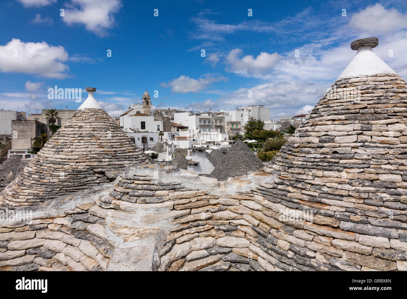 Trulli Roofs In The Foreground, Modern Part Of The City In The Background, Blue Sky, White Clouds, Alberobello, Province Bari, Apulia, Italy Stock Photo