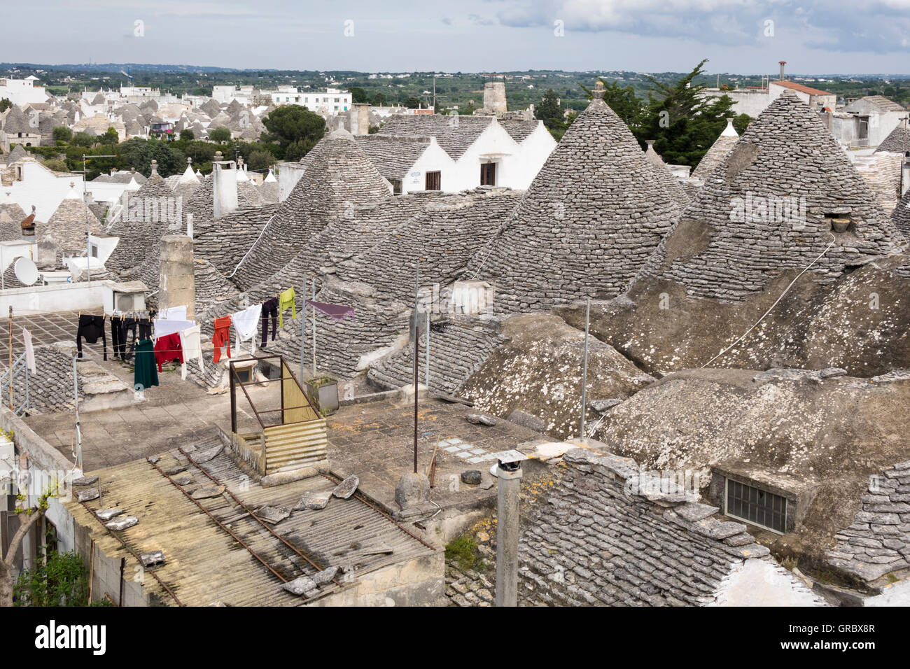 Trulli With Roofgarden In The Foreground, Modern Part Of The City In The Background.Alberobello, Province Bari, Apulia, Italy Stock Photo