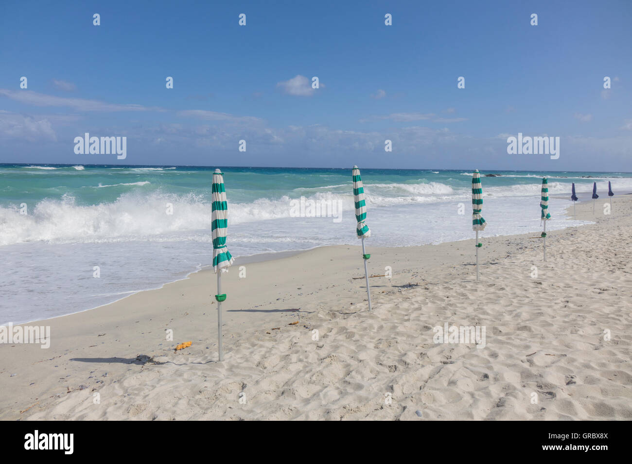 Deserted White Sandy Beach, Sunshades, Surge, Blue Sky And White Clouds Stock Photo