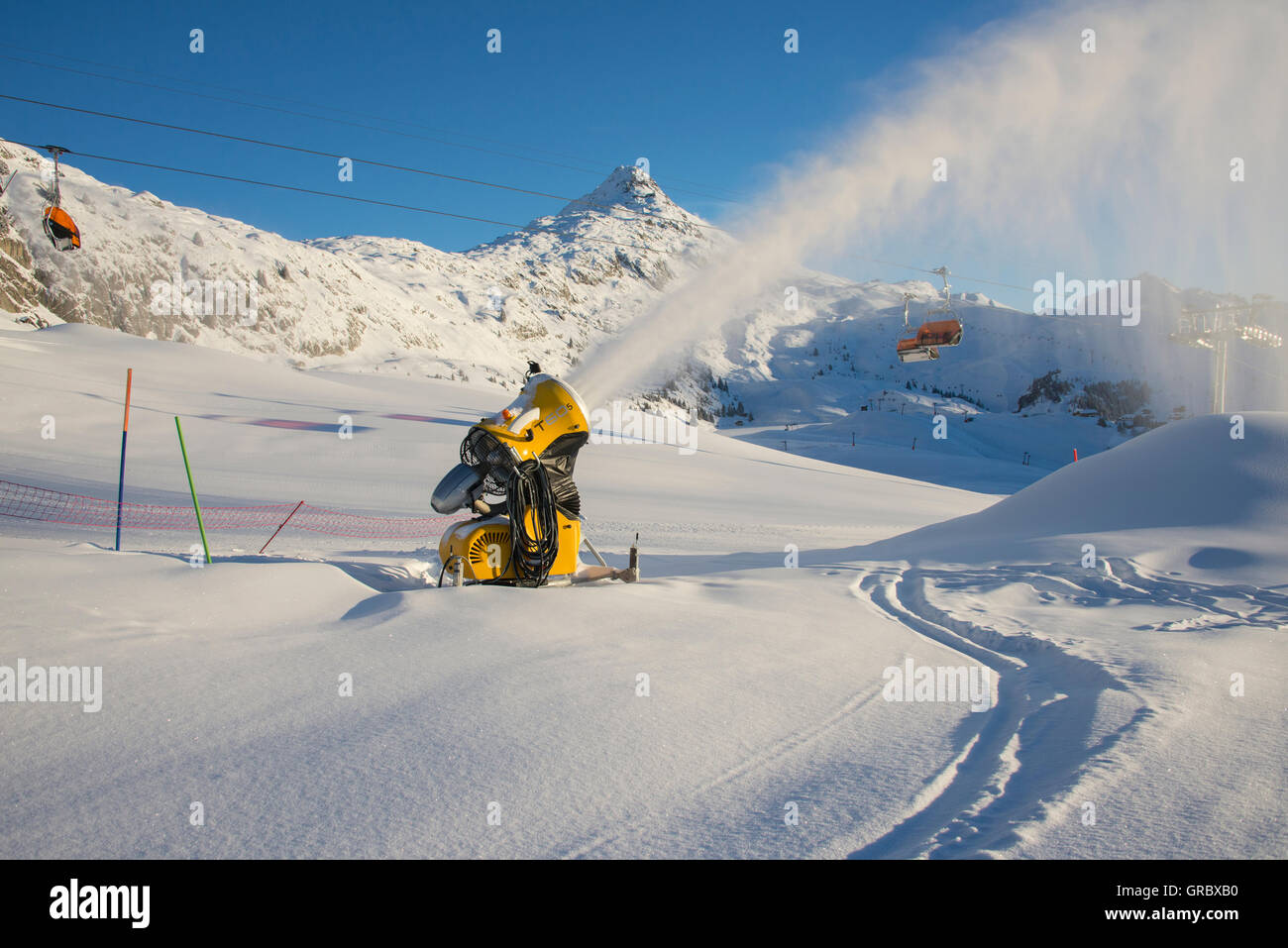 Snowfield With Active Yellow Snow Cannon, In The Background Bettmerhorn And Blue Sky Stock Photo