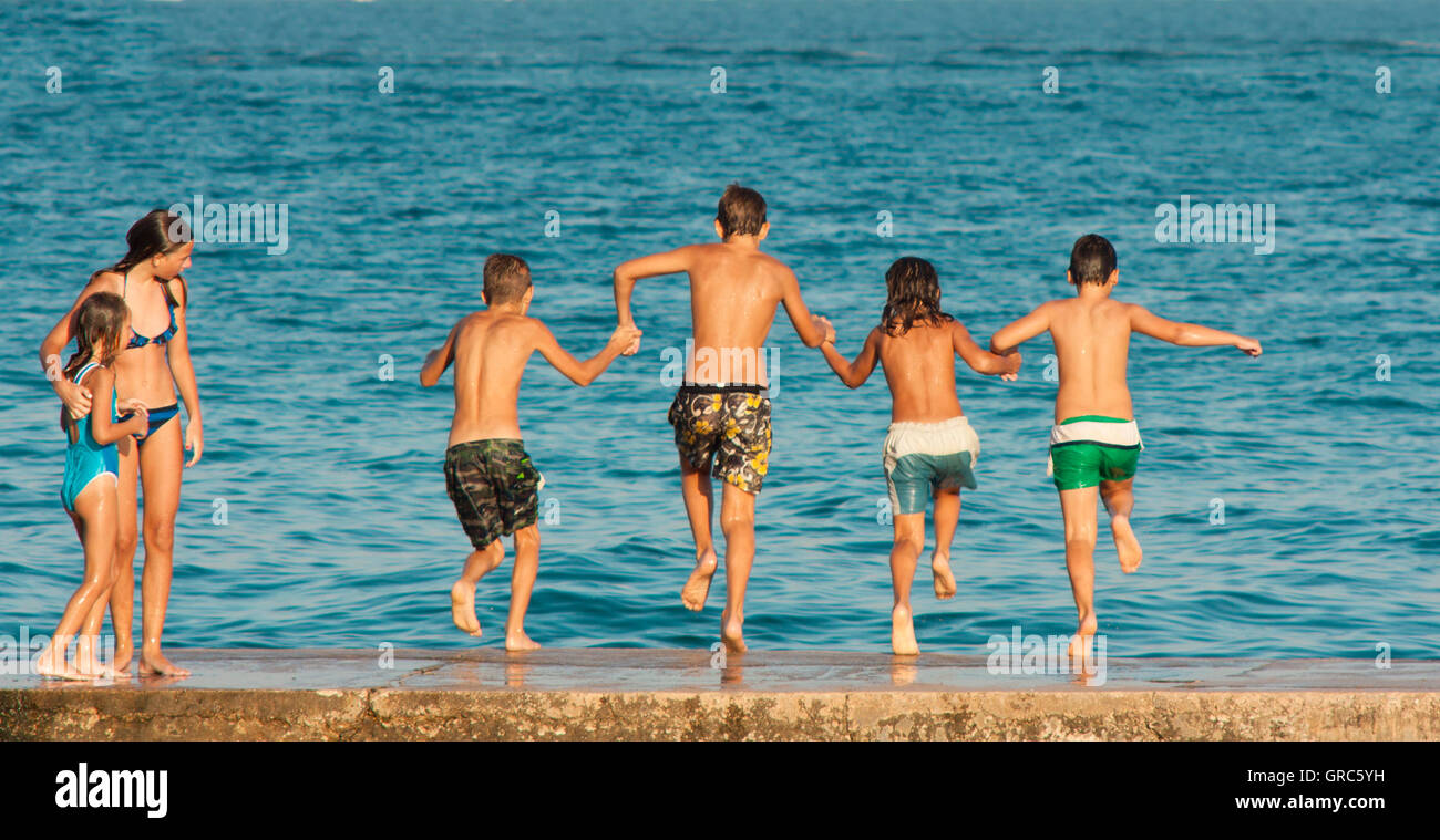 Vodice, Croatia - August 21, 2016: Two young girls watching four pre-adolescent boys holding hands while jumping into the sea. Stock Photo