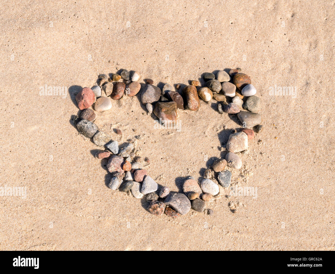 Heart sign arranged from pebbles on beach sand Stock Photo