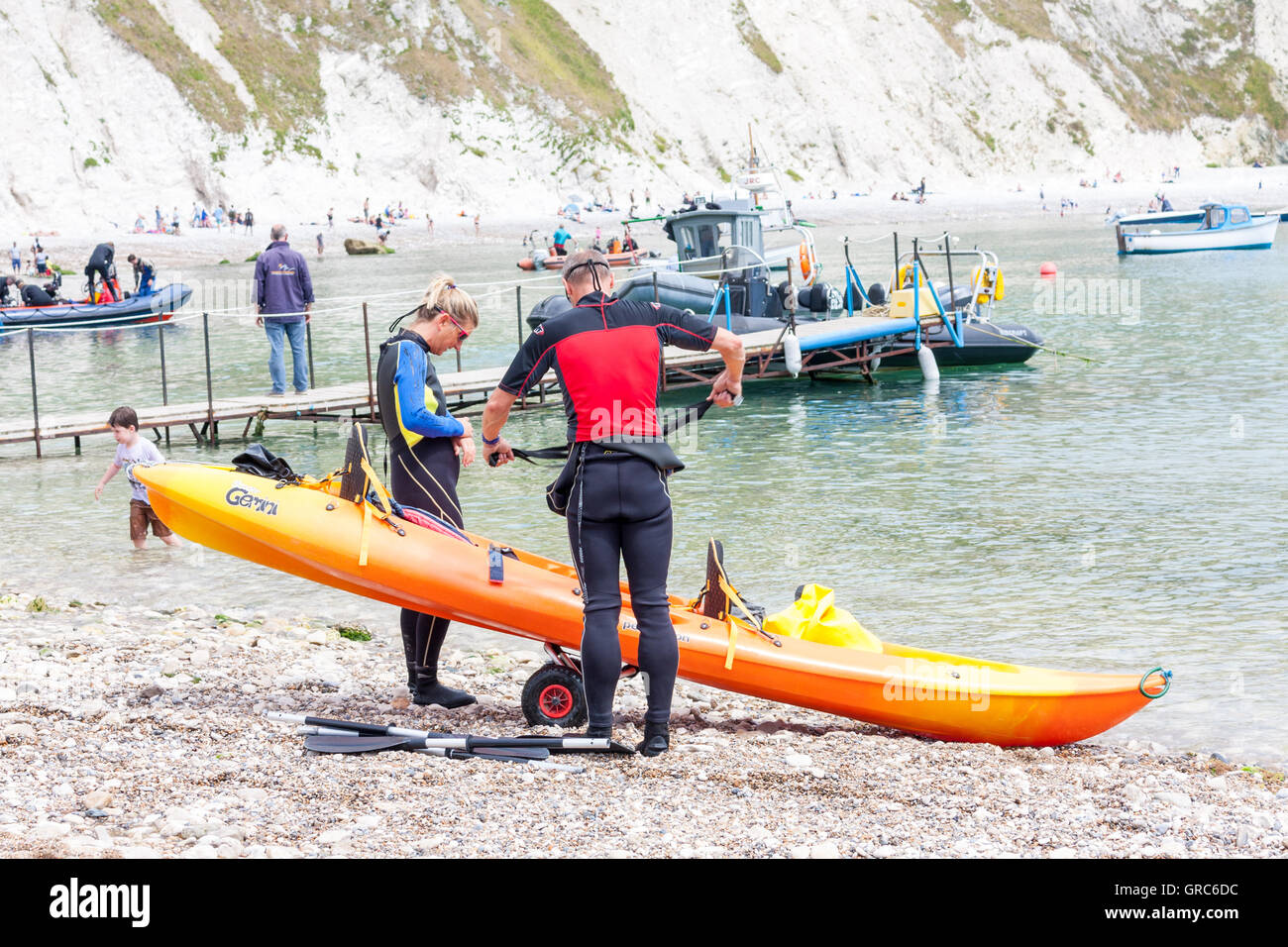 Two people preparing a canoe on the beach at Lulworth Cove, Dorset, UK