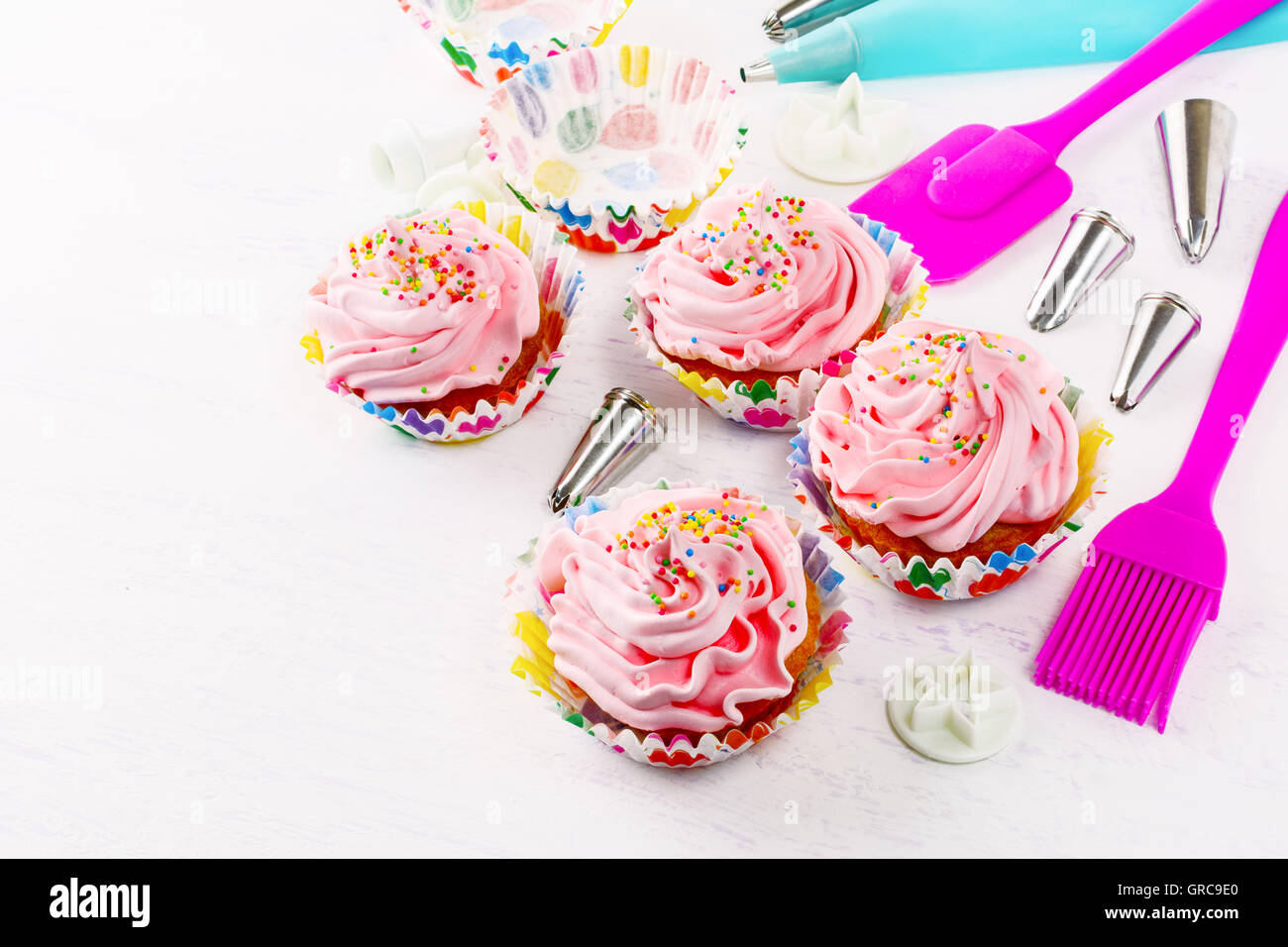 Decorated birthday cupcakes and cookware background. Birthday cupcake with pink whipped cream. Homemade party cupcakes. Stock Photo