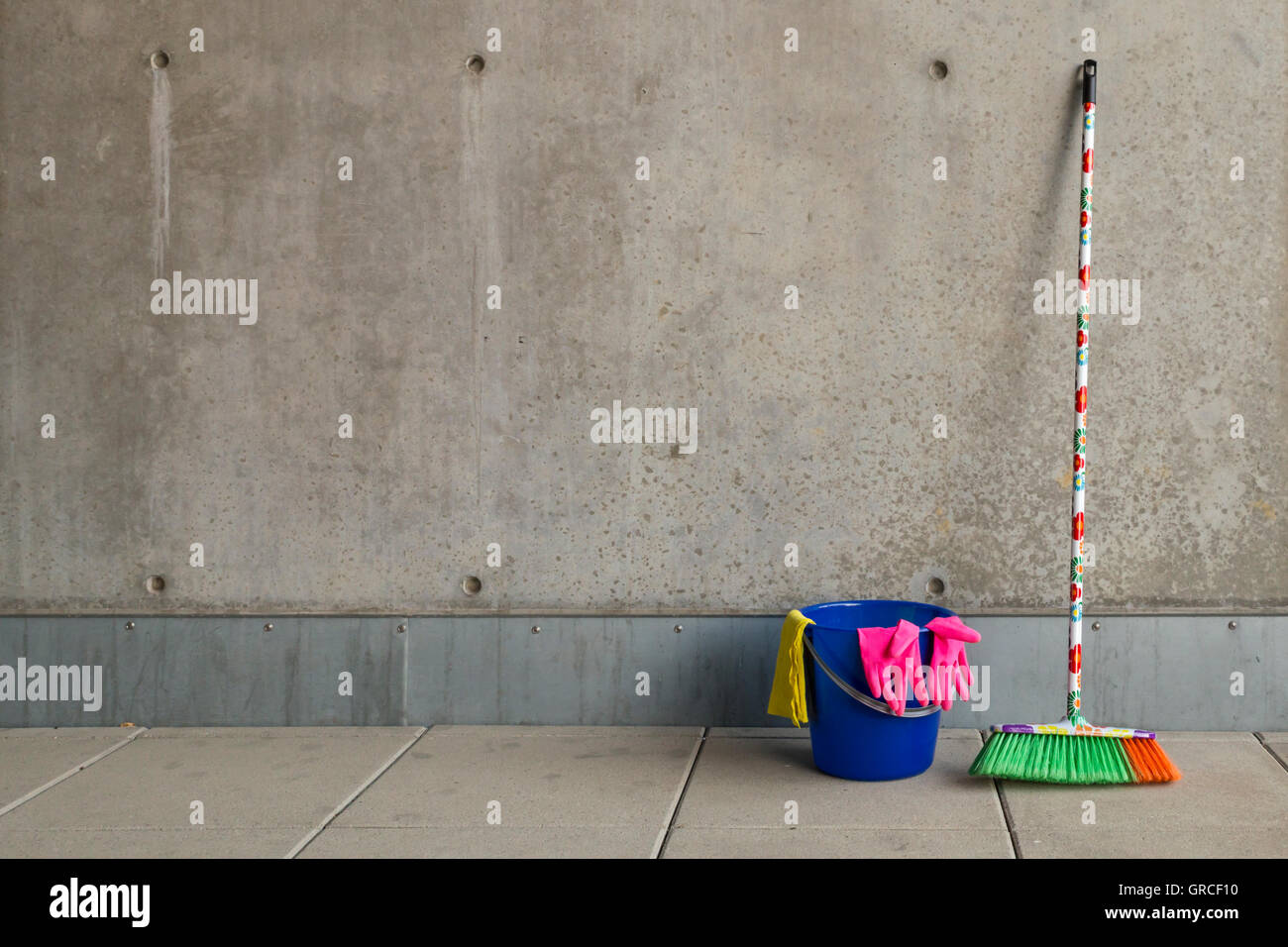 Colorful cleaning equipment (broom, bucket, rag and gloves) in front of