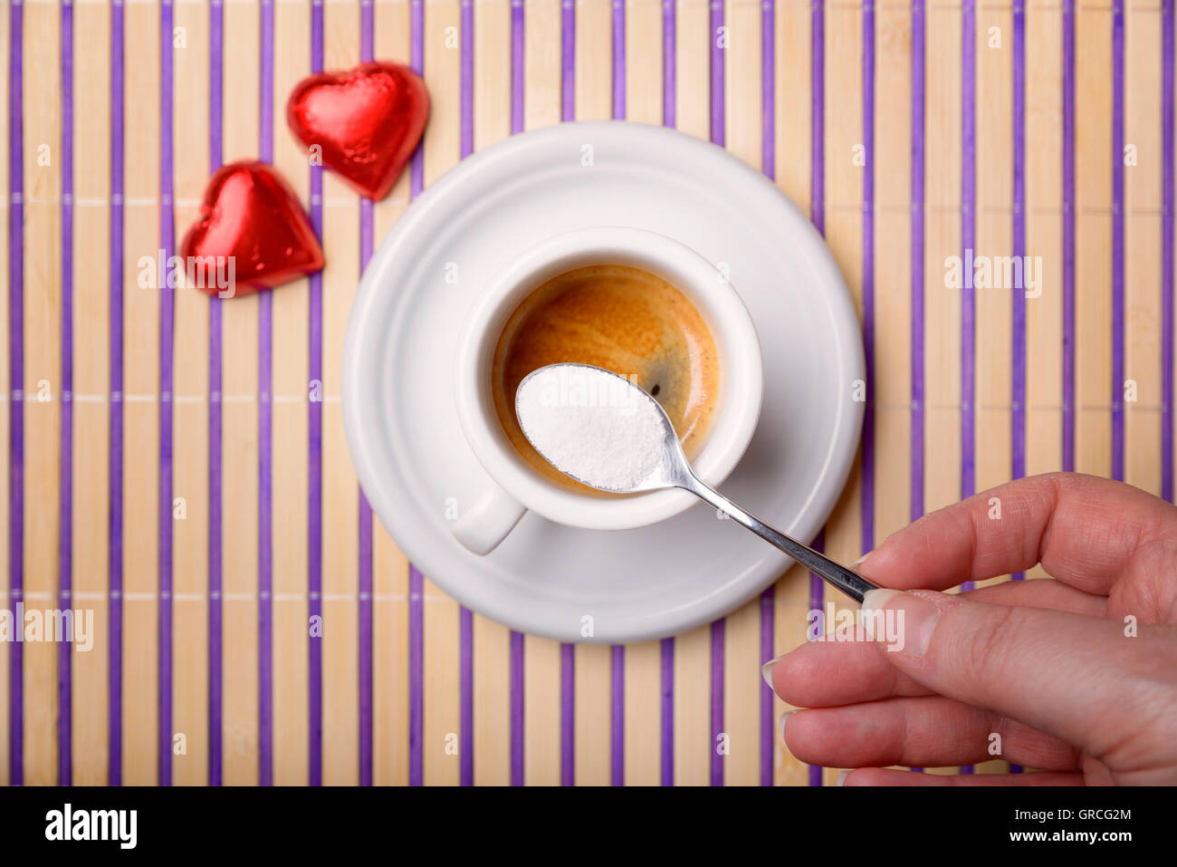 female hand with a teaspoon of sugar to sweeten a cup of coffee and two chocolate heart Stock Photo