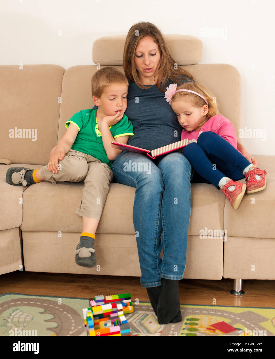 Mother reading fairytale book to her daughter and son in living room. Stock Photo