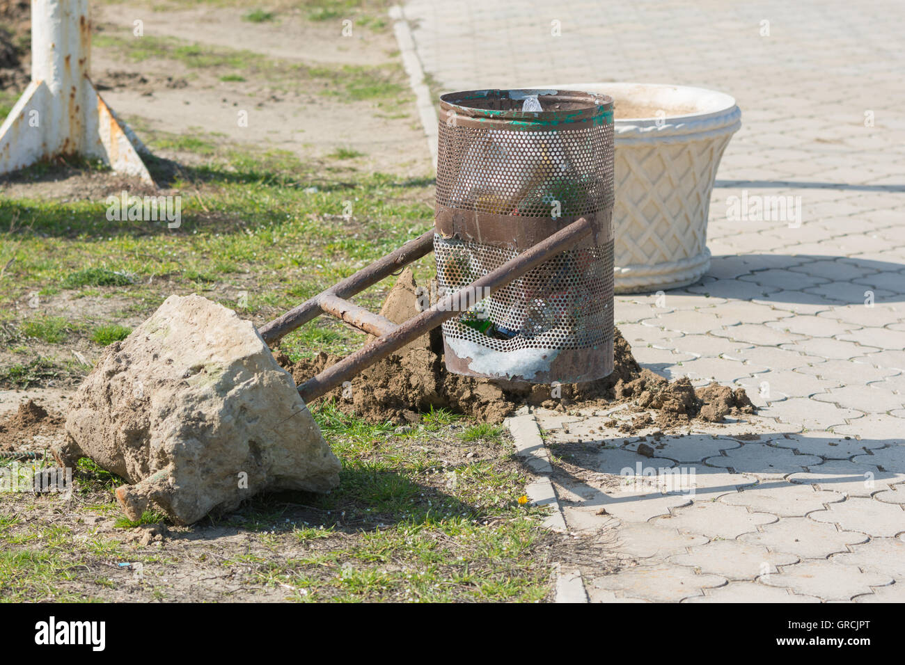 Torn out of the earth a broken wheelie bin with concrete base Stock