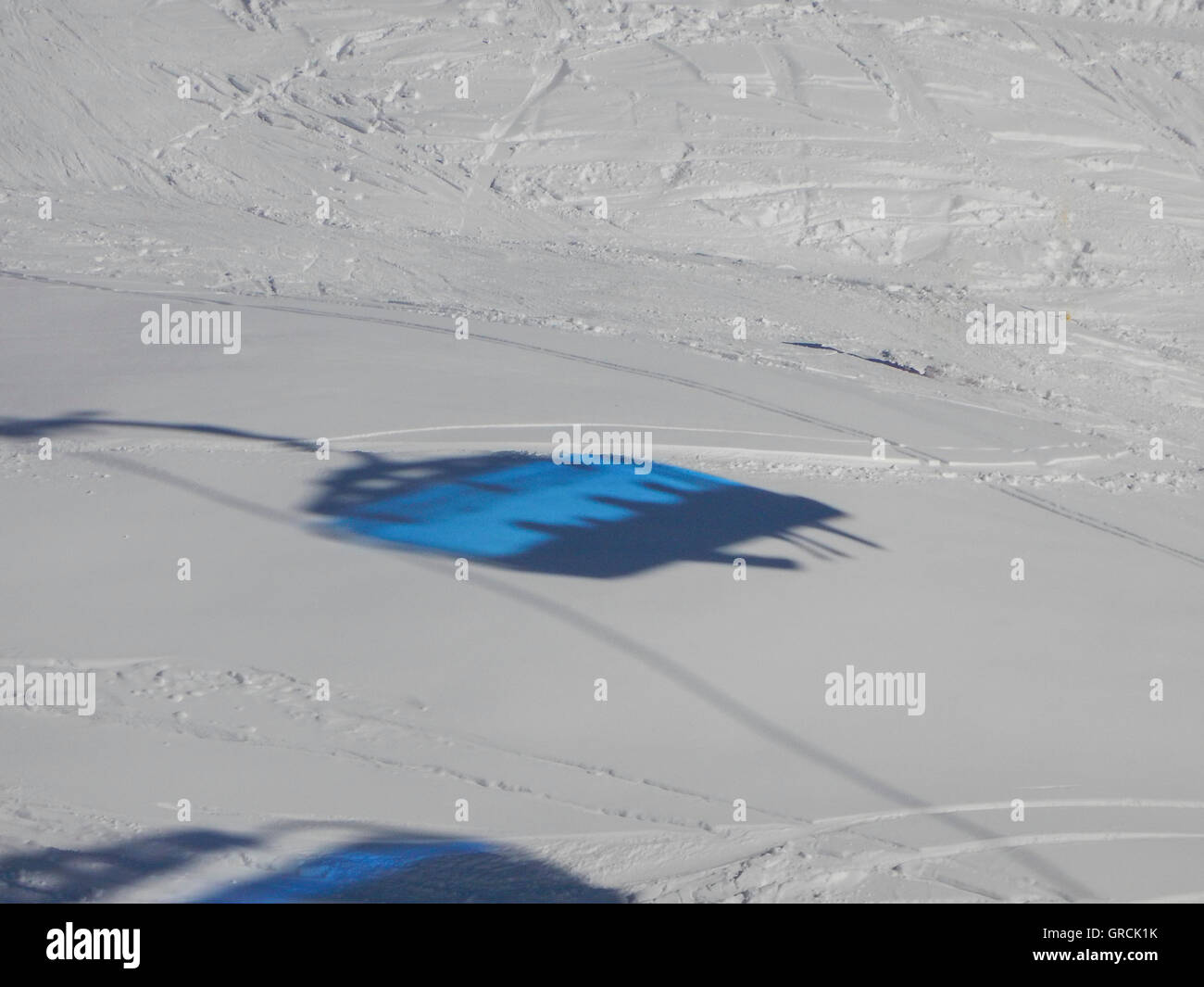 Blue Silhouette Of A Chairlift With Skiers On A White Snowfield With Ski Tracks Stock Photo
