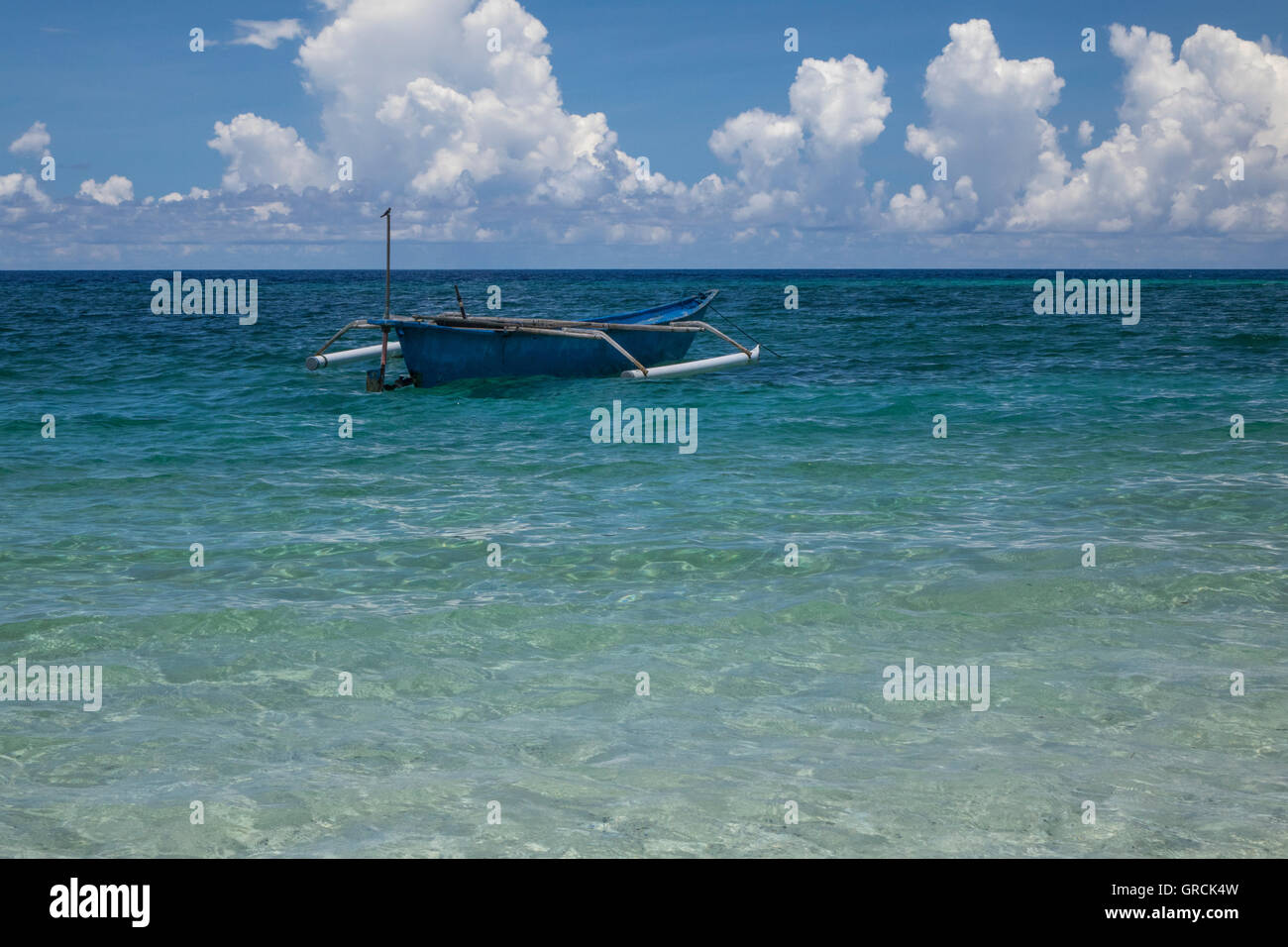 Indonesian Outrigger Canoe Near The Beach, White Cumulus Clouds And Blue Sky In The Background Stock Photo