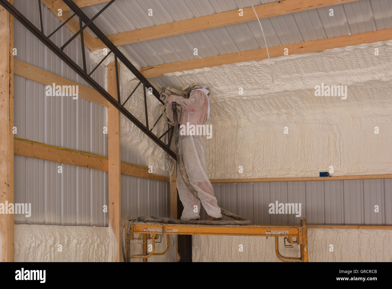 A technician applies open cell foam insulation to a structure's interior for sound control and energy conservation. Stock Photo