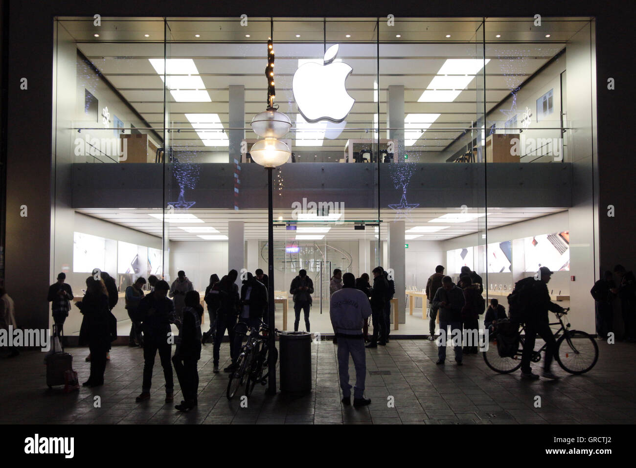 Group Of People Using Hot Spot At A Closed Apple Store In Munich At Night Stock Photo