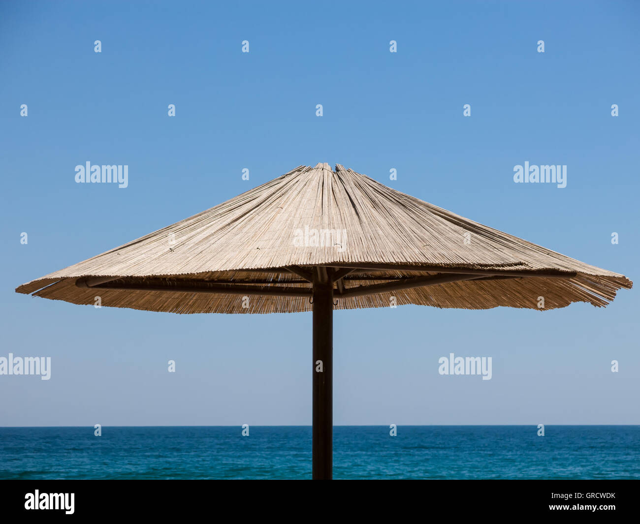 Upper Part Of A Single Sunshade Made Of Straw Against Blue Sky And Sea Stock Photo
