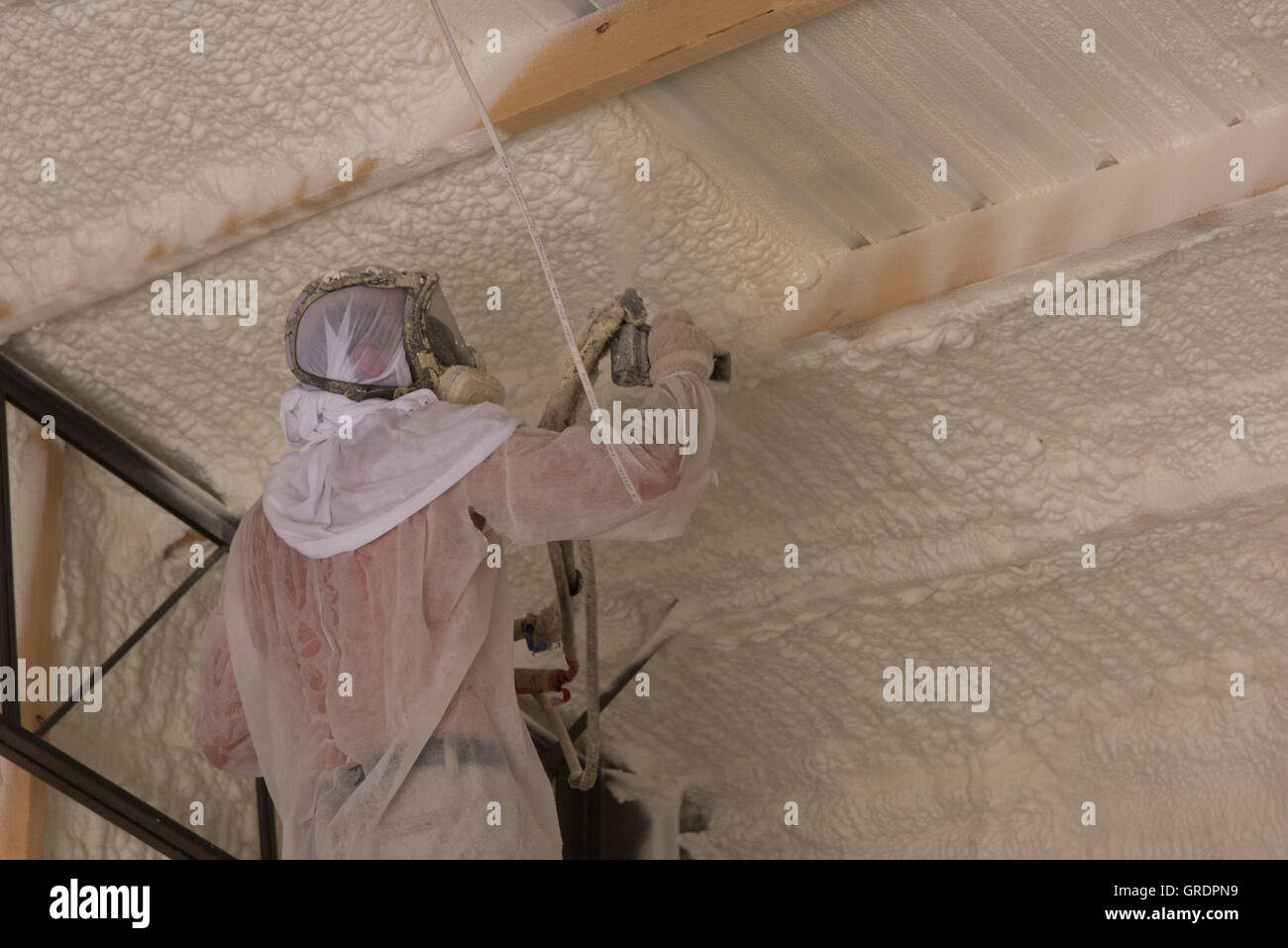 A technician applies open cell foam insulation to a structure's interior for sound control and energy conservation. Stock Photo