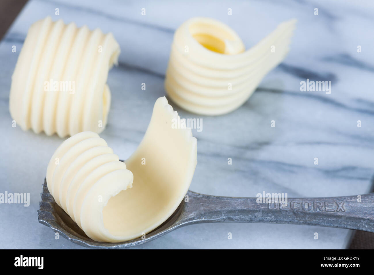 Three Butter Curls On A Marble Slab With Decorative Spoon Stock Photo