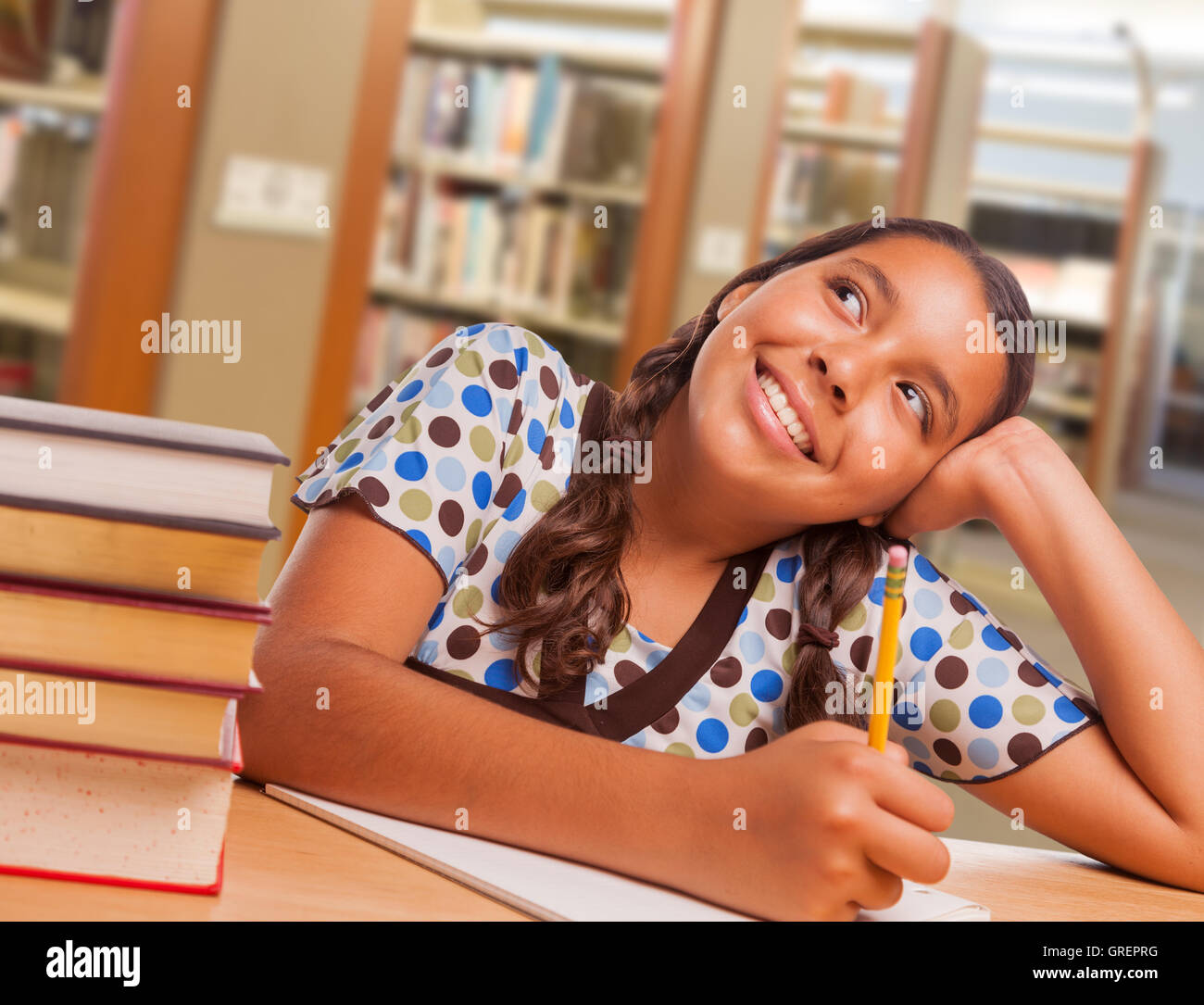 Happy Hispanic Girl Student with Pencil and Books Daydreaming While Studying in Library. Stock Photo