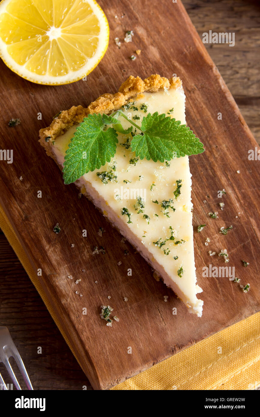 Piece of delicious homemade lemon cheesecake with mint on rustic wooden background close up Stock Photo