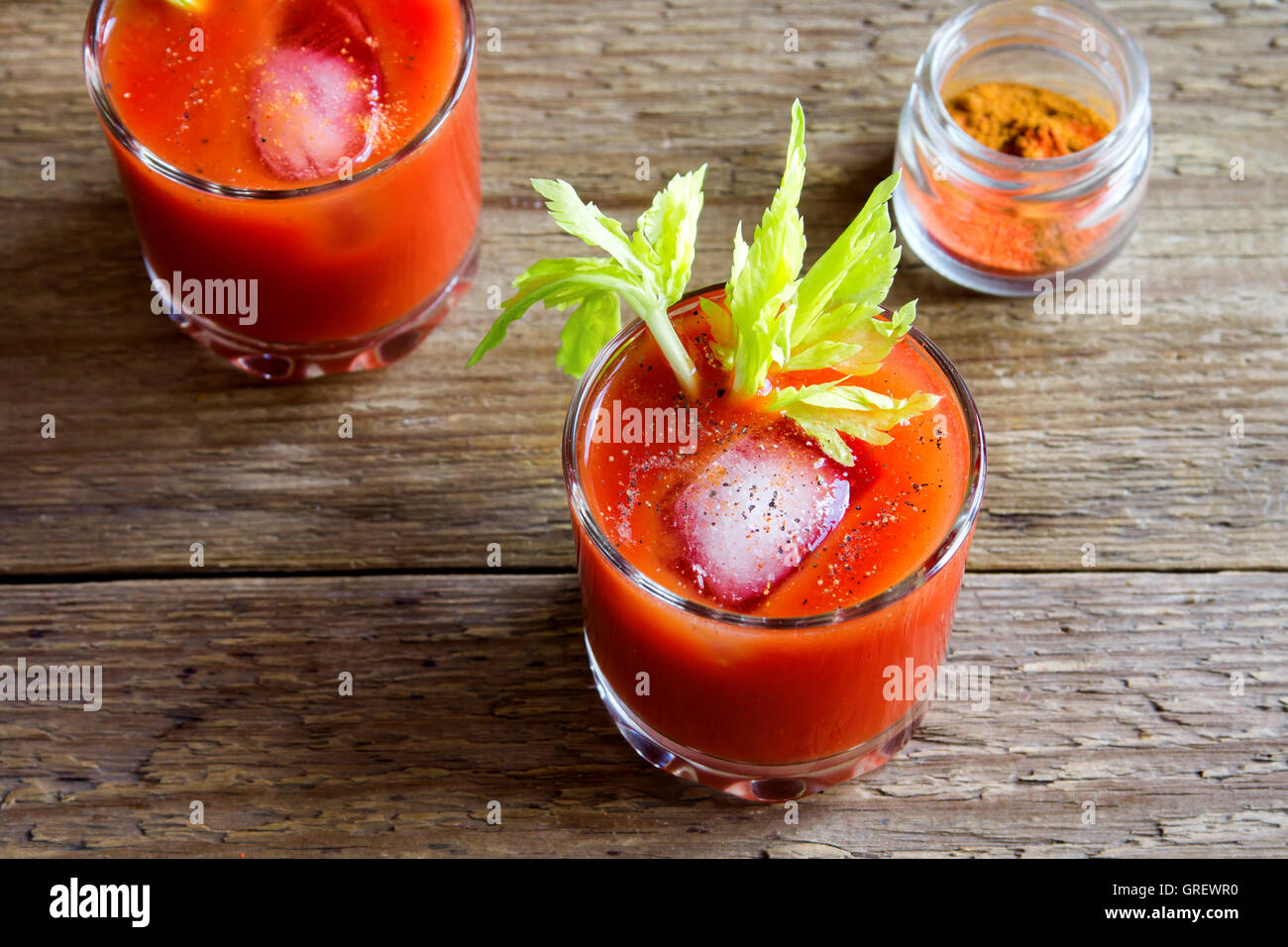 Tomato juice with celery, spices, salt and ice in portion glasses